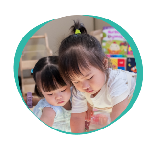 Two toddlers sitting close together, absorbed in an activity on the floor.